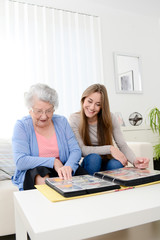 elderly woman with her young granddaughter at home looking at memory in family photo album