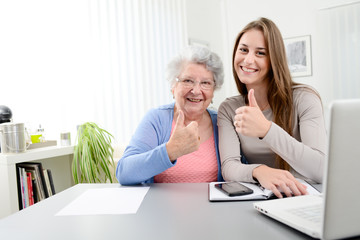 young woman helping an old senior woman doing paperwork and administrative procedures with laptop...