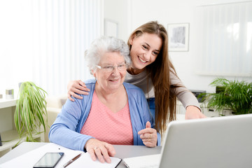 young woman helping an old senior woman doing paperwork and administrative procedures with laptop...