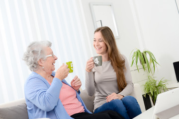 happy old senior woman spending time and drinking tea with cheerful young girl at home