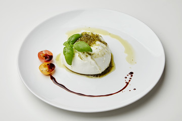 Mozarella served with pesto, cherry tomatoes and basil on white