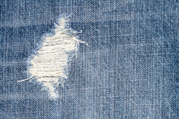 Close up texture of blue torn denim jeans with hole and threads