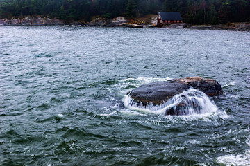 Water pooring of rock in ocean after a wave hit with forest and red house in soft focus background