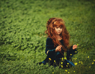 beautiful little girl with red hair and a bow and arrows in the green forest