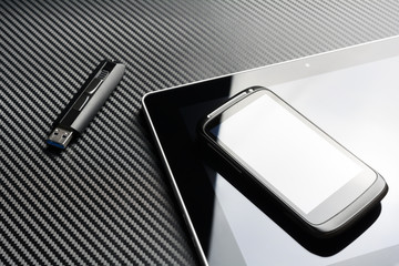 Blank Smartphone With Reflection Lying On Business Tablet Next To An USB Storage Flash Drive Above A Carbon Background