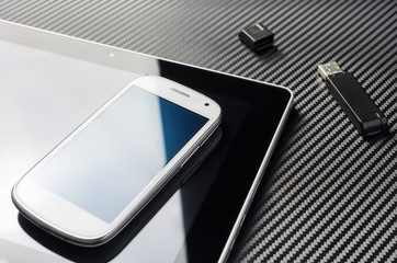 Blank Smartphone With Blue Reflection Lying On Business Tablet Next To An Open USB Storage Flash Drive Above A Carbon Background