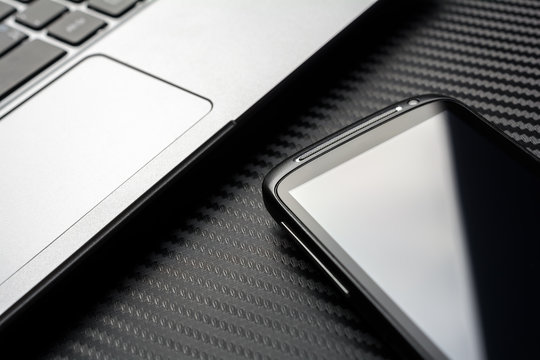 Blank Business Smartphone With Reflection Lying In Front Of A Notebook Keyboard, All Above A Carbon Background