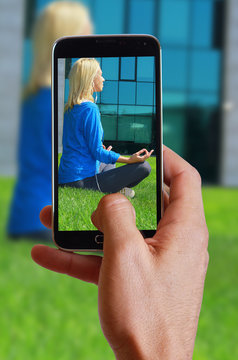 Male hand taking photo of Woman  meditating  in  City Central Park in yoga lotus pose with cell, mobile phone. Sport, fitness, active lifestyle , urban workout concept