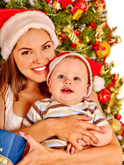 Mom wearing Santa hat holding  baby  under Christmas tree.