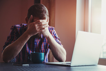 Stressed man with head in hands near laptop