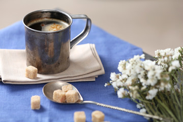Metal cup of flavored coffee with lump sugar and flowers on table with napkin, closeup
