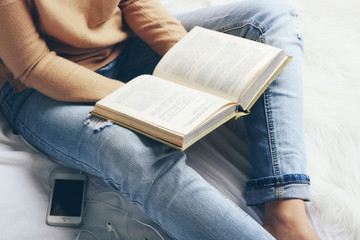 Obraz premium Woman in blue jeans reading book on bed top view point