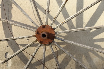 Wagon wheel.
Old wagon wheel leaning against a wall casting shadow. 
