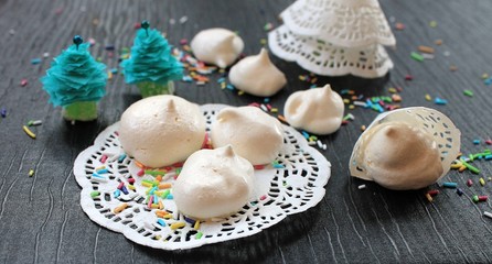 
Meringue cakes out of the egg white and sugar white lacy napkin on a black table in the New Year and Christmas decorations