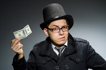Young man in black coat holding money against gray