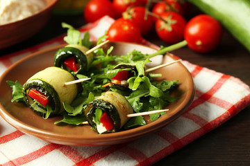 Zucchini rolls with cheese, bell peppers and arugula on plate, close-up, on table background