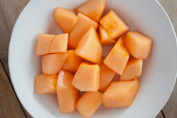 closeup melon slice in white dish with wood table background