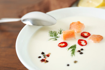 Delicious salmon cream soup with spoon on wooden table, close up