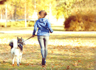 Naklejka na ściany i meble Happy young woman jogging with her dog in park