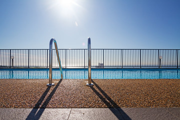 Edge of swimming pool with sun flare in background