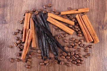 Fragrant vanilla, cinnamon sticks and coffee grains on wooden surface