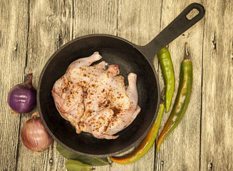 Raw fresh chicken on iron pan  with chili pepper and onions over wooden background.