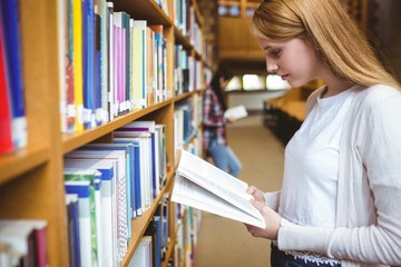 Blond student reading book in library
