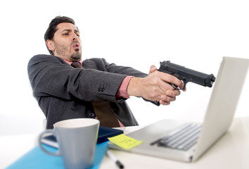 businessman in suit and tie sitting at office desk working on computer  pointing gun to laptop in...