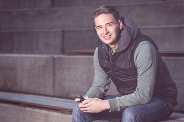 Young man with smartphone sitting on stairs