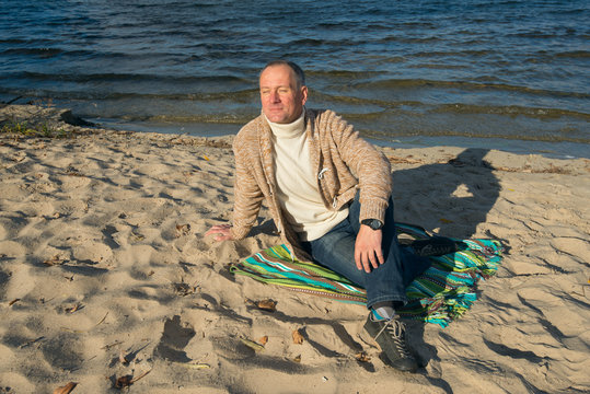 Joyful smiling man, wearing casually,sitting on the coast, looki