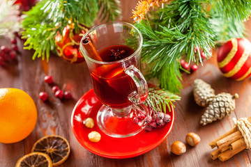 Fototapeta na wymiar Glass of traditional hot drink on table by Christmas tree with decorations. Mulled wine.