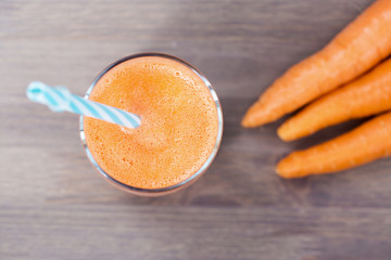 Healthy carrot smoothie in a glass with tube wooden background