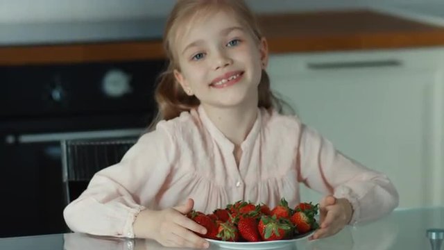 Girl pulling the large plate of strawberries and looking at camera