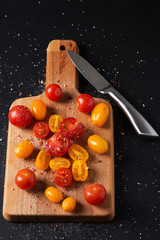 Different tomato cultivars on a wooden board on the black background. top view