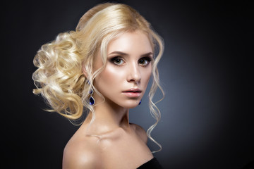 Beautiful blond girl in a black dress with evening haircut  form of waves and bright makeup. Beauty face