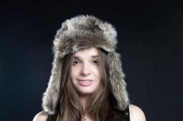 Portrait an attractive girl in fur hat on black background