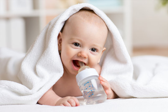 Adorable baby boy drinks water from bottle wrapped towel after bath