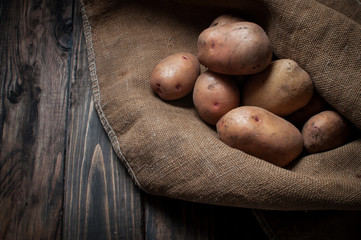 Harvest potatoes in burlap sack on wood background.