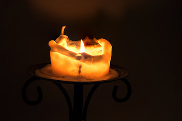 white candle with flame and melting wax on an iron candlestick a