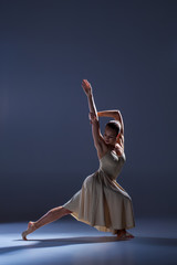 Fototapeta premium Young beautiful dancer in beige dress dancing on gray background