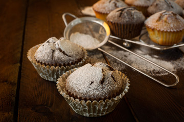 Vanilla and chocolate muffins, caster sugar, sieve for a baking on a dark background, selective focus, copyspace