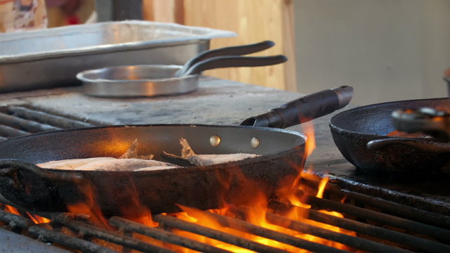 The fish in the pan is grilled on a big fire on the grill. 