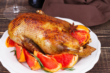 Festive Christmas duck baked with grapefruit and rosemary, glass and bottle of red wine; candles