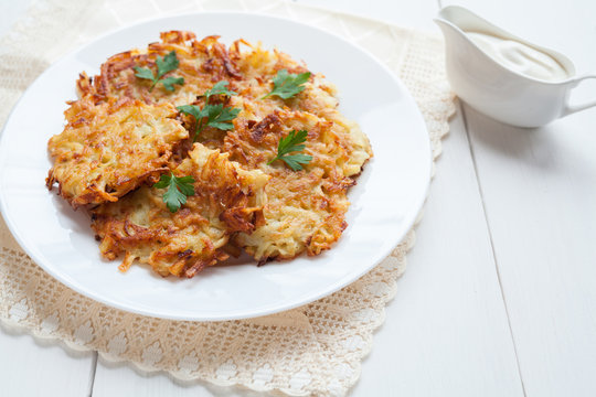 Potato pancaces or latke traditional Hanukkah celebration food with sour cream on white rustic background. Vegan organic meal