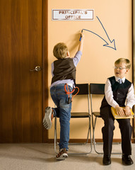 Schoolboys are sitting beside the principal's office in school
