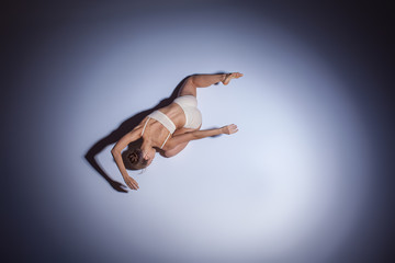 Young beautiful dancer in beige swimwear dancing on lilac background