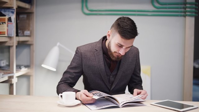 Nerd hipster guy with glasses sitting at bar table and using a tablet