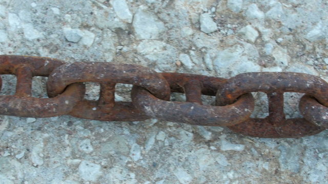 A big chain lying on a snowy ground. It is a rusty chain on the ground