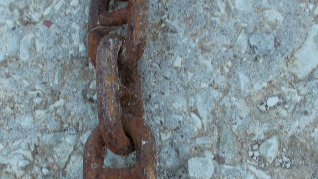 Red big chain on the white rock ground. The chain is connected maybe on an anchor of a big boat