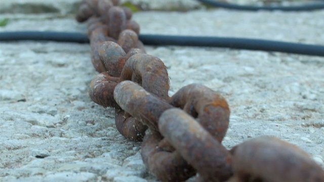 A red big chain from a big anchor of a ship. It is a rusty chain on the rocky ground in a small port